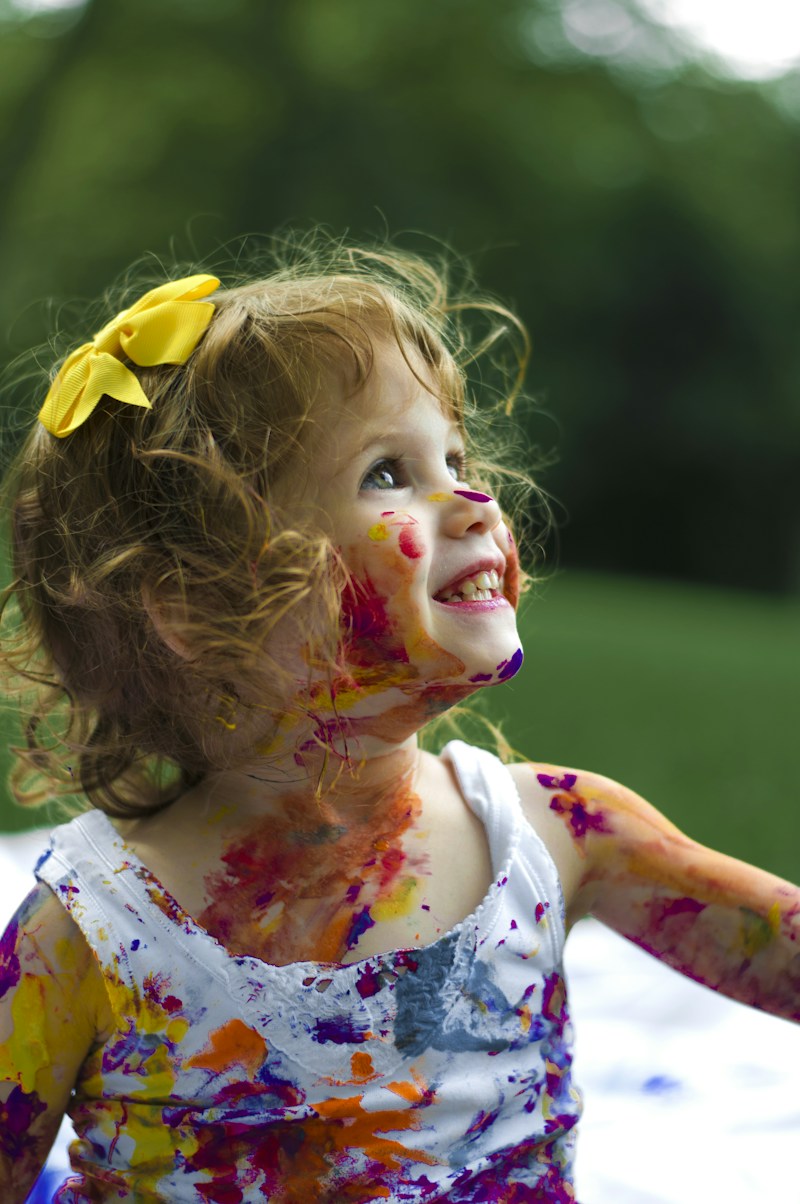 A smiling toddler with colorful paint on her hands and face